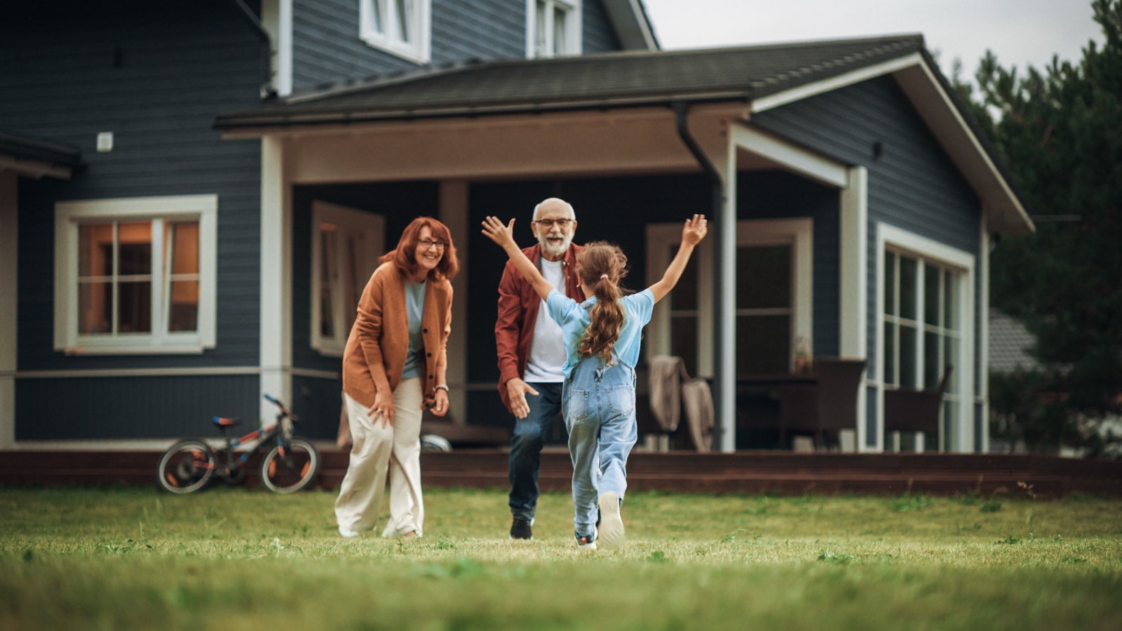 A grandfather and grandmother in their late sixties greeting their grandchild in the backyard of their home, warm and well